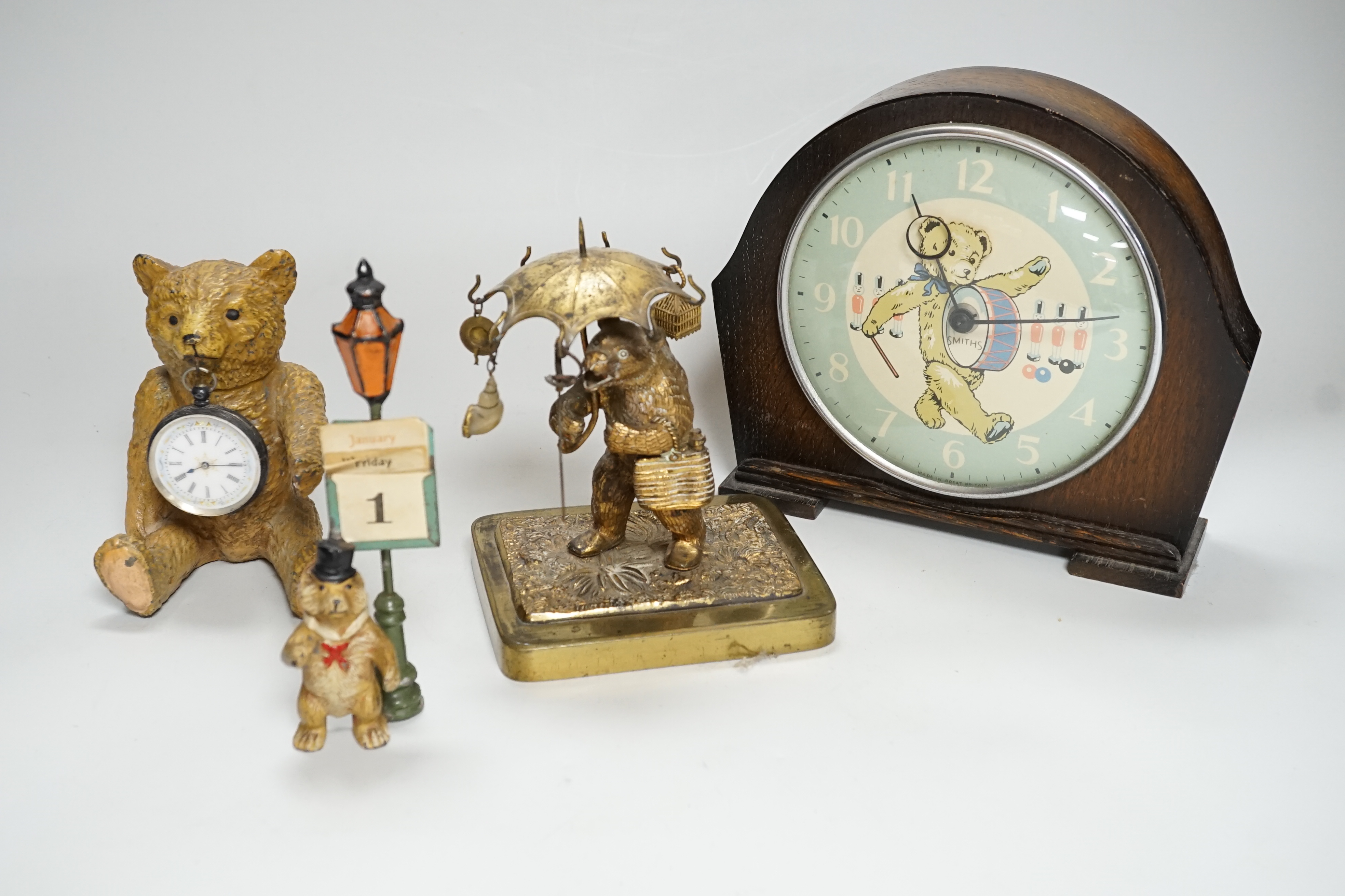 A Smith teddy bear clock, a seated metal bear holding a pocket watch, a metal standing bear with parasol and a German metal bear calendar